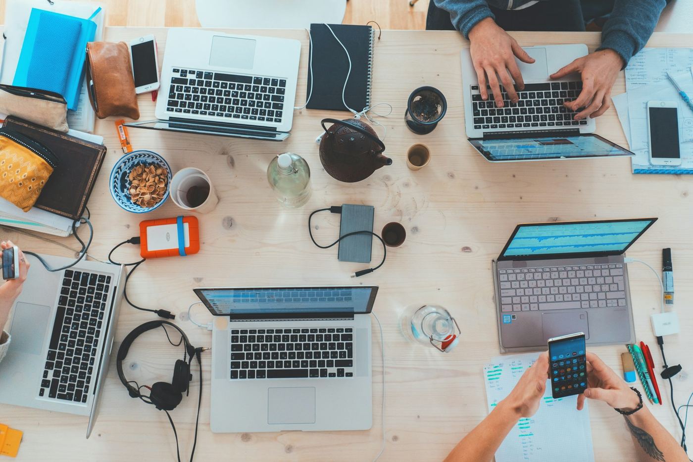 Overhead view of a shared desk with laptops, headphones, phones, and notebooks